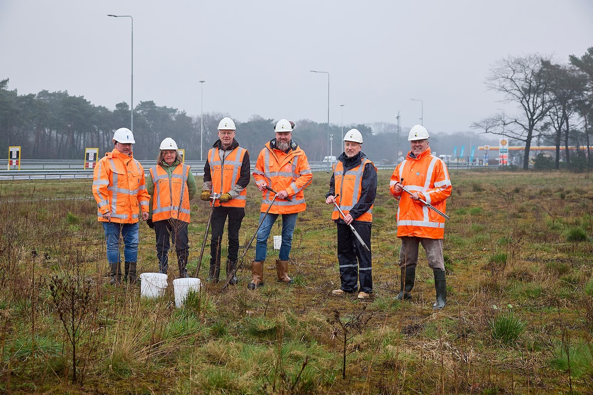 Zes projectpartners in oranje werkkleding en met witte helmen staan naast elkaar in het veld aan de snelweg A58.